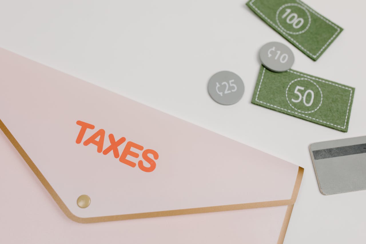 Pink envelope labeled TAXES with play money and card on white background.